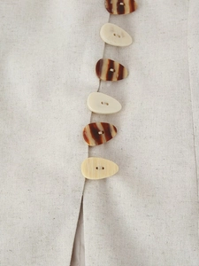 Close-up of irregular pebble-shaped buttons on linen blend fabric with woven texture