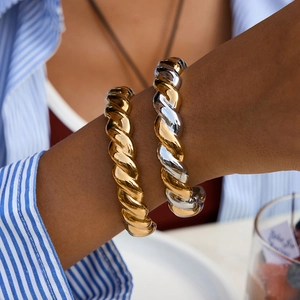 Detail of twisted croissant bangles in gold and silver finish on model's wrist