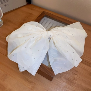 Detail of a white mesh bow hair clip with silver dots on a wooden jewelry display tray