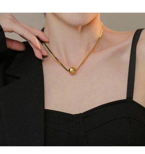 Detail of a double-layered gold snake chain necklace with a polished spherical pendant