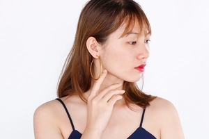 Macro detail of large gold hoop earring worn by a model against a white background