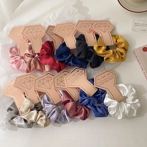 Set of 11 colorful silk satin scrunchies with stylish packaging on a white textured background