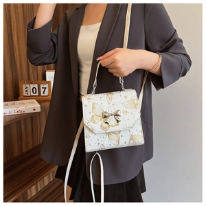 Detail of white PU bag with gold butterfly prints and a metallic 3D bow clasp