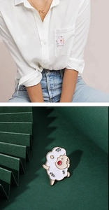 Detail of white lamb enamel brooch on white shirt and green pleated background