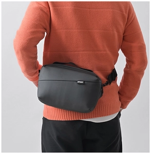 Close-up of black crossbody bag with sport tag worn over an orange textured sweater