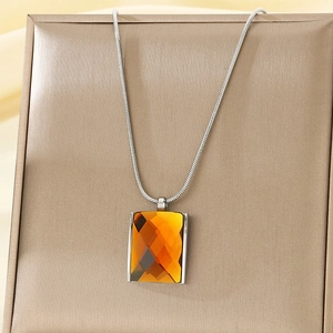 Detail of silver snake chain with rectangular amber gemstone pendant on golden texture box
