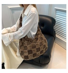 Close-up of brown checkerboard plush shoulder bag held by a model on a leather sofa