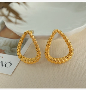 Detailed close-up of gold drop earrings with textured twist rope design on ceramic plate