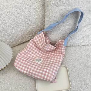 Detail view of pink plaid canvas tote bag with light blue strap on a plush white surface
