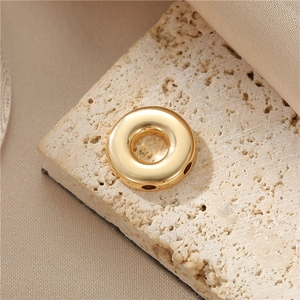 Polished gold donut-shaped metal jewelry pendant accessory displayed on a beige stone
