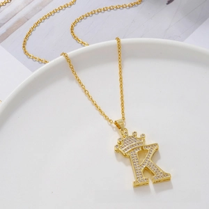 Detailed view of gold crown letter K pendant with sparkling crystals on white tray
