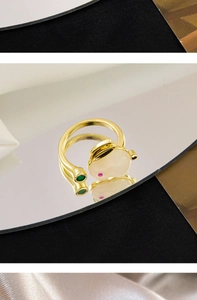 Detail of adjustable gold-plated ring with white rabbit and green gemstone on silk