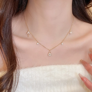 Detail of gold-plated necklace with key, cross lock, pearl and zirconia charms on a model