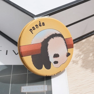 Portable round yellow leather makeup mirror with panda illustration on a wooden desk