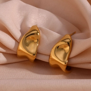 Detailed macro view of irregular wavy gold earrings on luxury champagne satin fabric