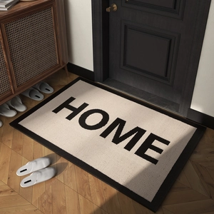 Rectangle cream HOME door mat with black border on wooden floor near dark door