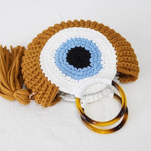 Macro shot of a handmade crochet shell bag with a blue evil eye pattern and brown tassel