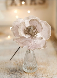 Close-up of pink artificial magnolia flower with gold glitter edges in a glass vase