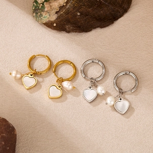 Detail shot of heart-shaped pearl drop earrings in gold and silver on a beachy background