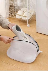 User placing white sneaker into mesh laundry bag for washing machine protection