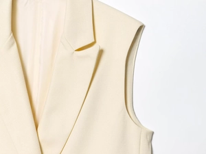 Détail du gilet sans manches blanc crème montrant le tissu texturé et le col à revers