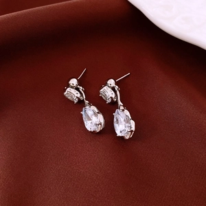 Detail shot of silver teardrop zircon earrings on premium red silk background