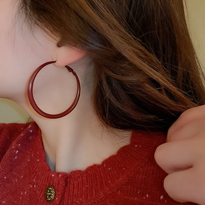 Close-up of a model wearing large glossy red geometric hoop earrings with a vintage style