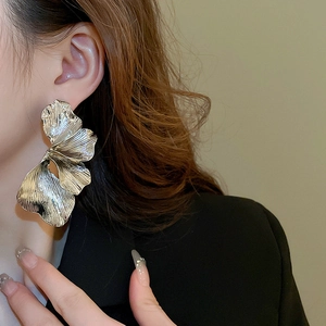 Macro side view of a large silver metal floral earring worn by a model on a warm background