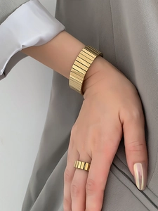 Close-up of golden grooved cuff bracelet and matching ring on model with grey suit
