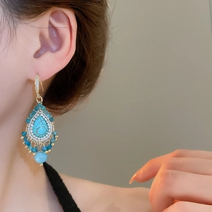 Close-up of teardrop turquoise tassel earring with diamonds and pearls on model