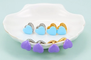 Detailed view of light blue and lavender enamel heart earrings on a shell tray