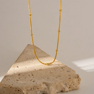 Minimalist gold snake chain necklace with beads displayed on a stone stand