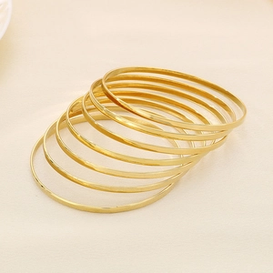 Set of 7 minimalist thin gold stainless steel bangles layered on beige fabric