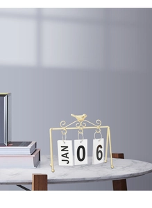 Close-up of golden bird desk calendar with flip cards on white marble tabletop