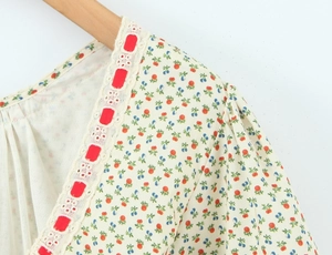 Detail van V-hals met rood lint, kant en bloemenprint van bessen op een beige jurk