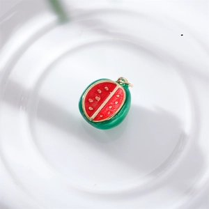 Detail of red and green enamel watermelon charm on a white ceramic tray for DIY jewelry