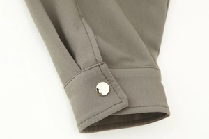 Close-up of taupe bomber jacket sleeve featuring a round silver metal snap button