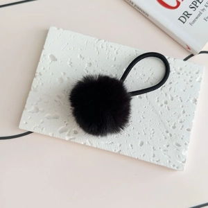 Close-up of fluffy black faux fur pom-pom hair tie on a white textured stone surface