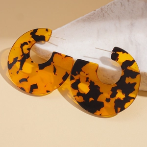 Artistic tortoiseshell acrylic C-shape hoop earrings resting on a white textured stone