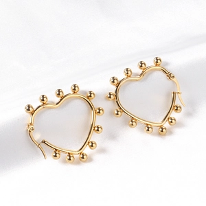 Polished gold heart hoop earrings with beaded edges on elegant white silk background