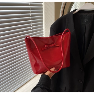 Close-up of red patent leather tote bag featuring a decorative bow and slim shoulder strap