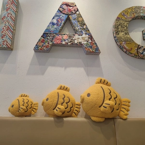 Three plush fish pillows in various sizes with curly fleece texture on a brown surface
