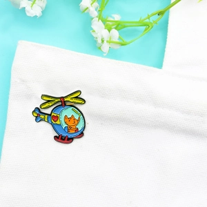 Broche en émail chat orange pilotant un hélicoptère bleu sur un fond bleu clair frais