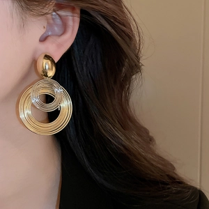 Close-up of model wearing gold multilayer geometric hoop earrings with layered metal coils