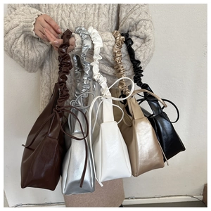 Detail of scrunchie handle and side bow knot on trendy pleated PU leather underarm bags