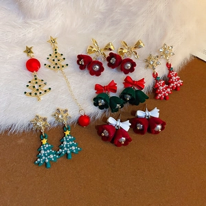 Set di orecchini natalizi con fiocchi di neve e alberi su superficie in peluche bianca