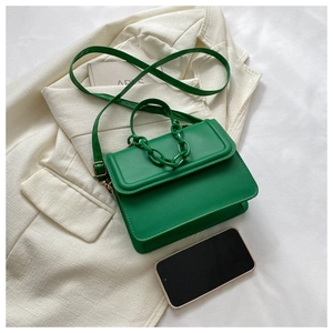 Detailed flat lay of a green PU leather crossbody bag with chain handle and stylish props