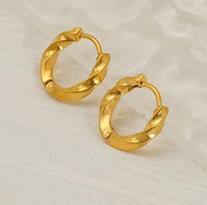Detailed shot of gold-plated twisted hoop earrings on a light luxury textured background
