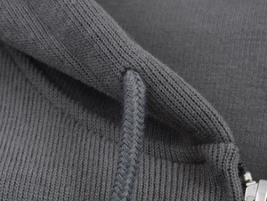 Detailed close-up of grey ribbed knit hoodie fabric with woven drawstring and metal zipper