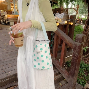 Close-up of white canvas mini bag featuring green polka dots and lace trim decoration